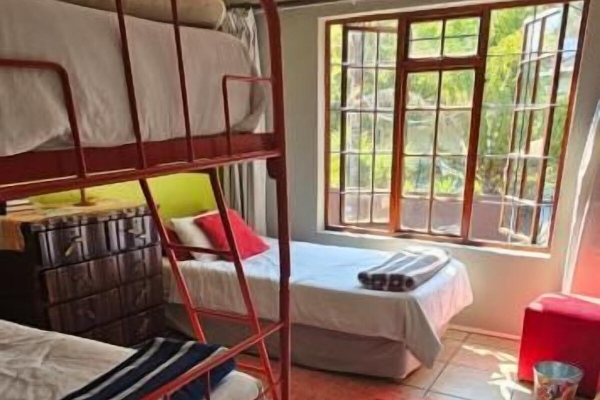 A room with bunk beds, a ceiling fan, a window with a view, and a red chair.