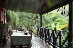An outdoor dining area with a table and chairs, surrounded by lush greenery and a wooden deck. - Old Vic Travellers Inn (Mbombela)