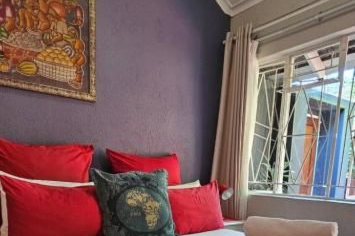 A bed with red and green pillows, a beige blanket, and a window with curtains.