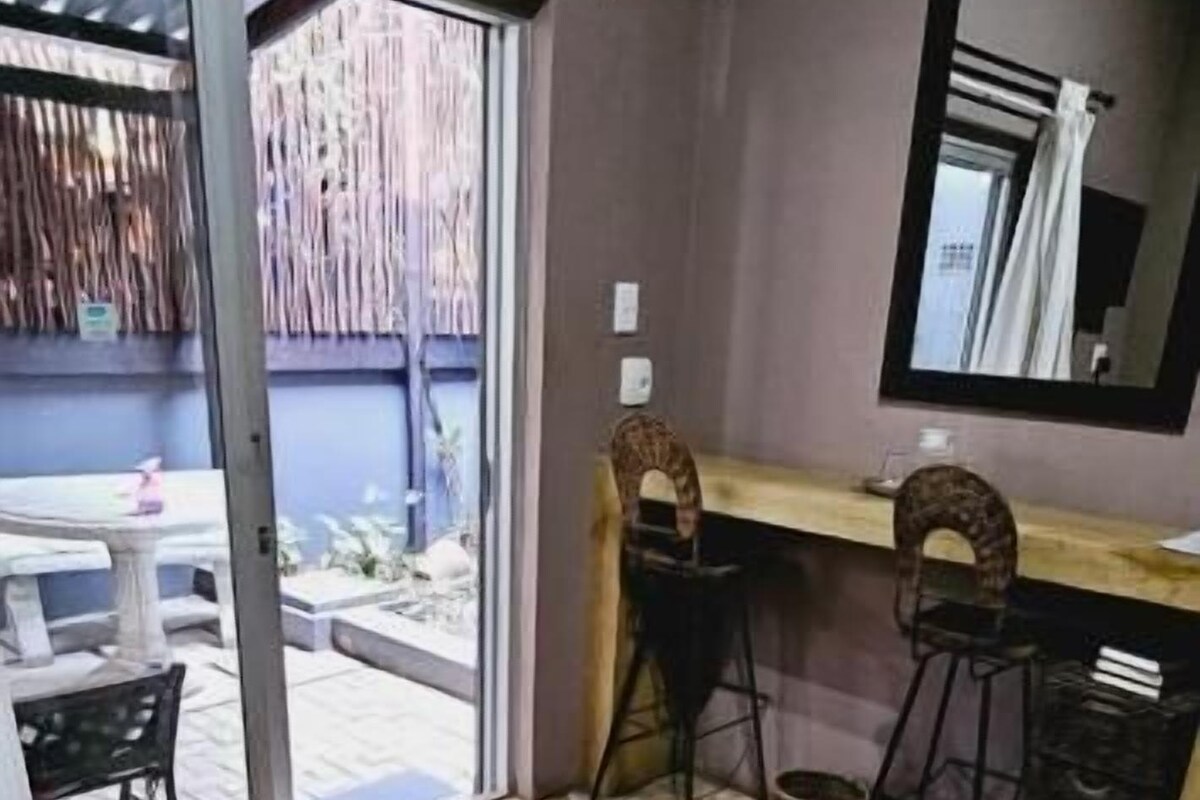 A hotel room with a bed, a desk, a chair, and a sliding glass door leading to an outdoor area.