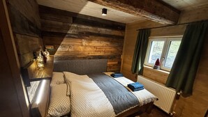 A wooden cabin bedroom with a bed, a window with curtains, and a radiator. - LostGarden Öblarn Top 1 (Öblarn)