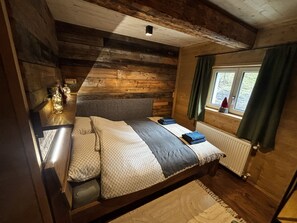 A wooden cabin bedroom with a bed, a window with curtains, and a radiator. - LostGarden Öblarn Top 1 (Öblarn)