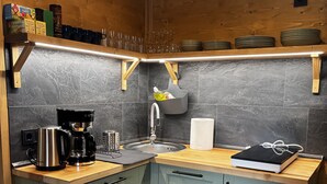 A kitchen with a wooden countertop, a coffee maker, a sink, and a shelf with plates and glasses. - LostGarden Öblarn Top 1 (Öblarn)