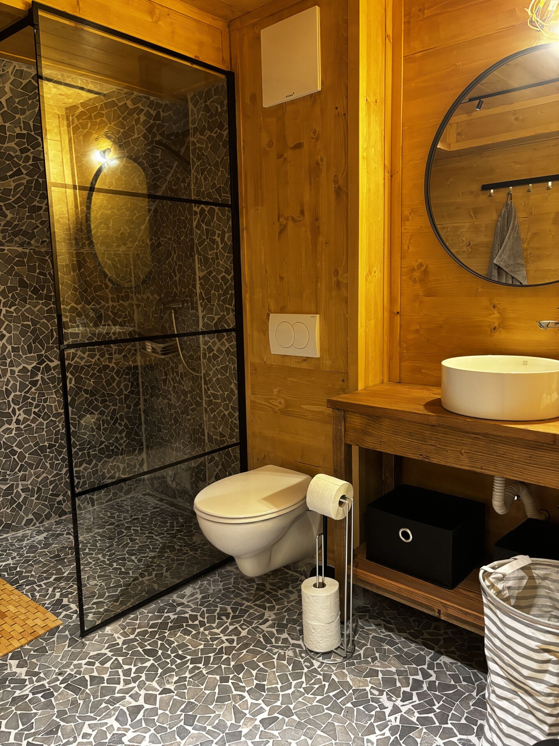 A bathroom with a mosaic floor, a toilet, a sink, and a shower with a glass door.
