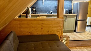 A cozy loft-style room with a sectional sofa, a small round table, and a kitchen area with a microwave and refrigerator. - LostGarden Öblarn Top 3 (Öblarn)