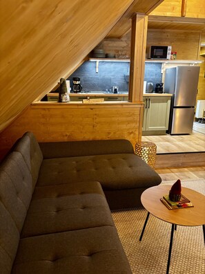 Ein gemütliches Loft mit Ecksofa, einem kleinen runden Tisch und einer Küchenzeile, inklusive Mikrowelle und Kühlschrank.
