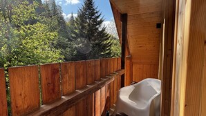 A wooden balcony with a wooden fence, a white bathtub, and a table with two glasses and a bottle. - LostGarden Öblarn Top 3 (Öblarn)