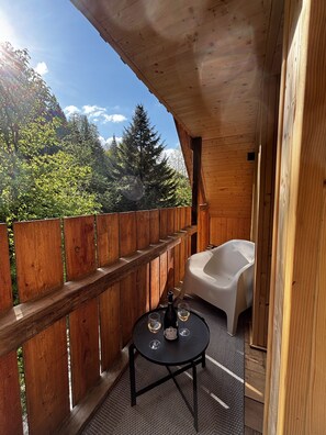 Ein Holzbalkon mit Holzzaun, einer weißen Badewanne und einem Tisch mit zwei Gläsern und einer Flasche.