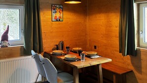 Een houten interieur met een eettafel voor vier personen, een stoel, een hanglamp en een raam met gordijnen.