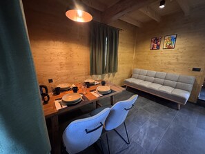 A dining area with a wooden table set for four, a grey sofa, and two white chairs. - LostGarden Öblarn Top 2 (Öblarn)