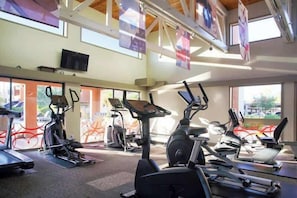 Ein Fitnessstudio mit mehreren Laufbändern und Ergometer, großen Fenstern und einer hohen Decke mit freiliegenden Balken.