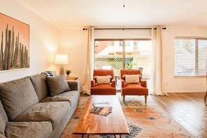 Ein Wohnzimmer mit einer Couch, zwei Sesseln, einem Couchtisch, einer Lampe und einem Gemälde an der Wand.