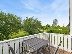 A balcony with a table and chairs, surrounded by white railings, overlooking a green landscape with trees and a hedge. - Cozy holiday home by the Baltic Sea for groups (Bastorf)