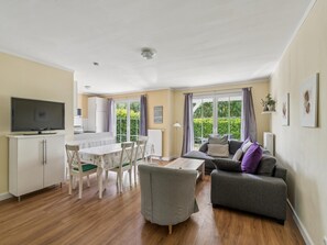 A modern living room with a sofa, a dining table, and a TV. - Cozy holiday home by the Baltic Sea for groups (Bastorf)