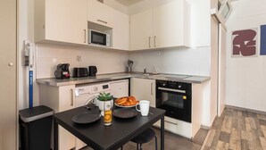 Une cuisine compacte avec des meubles blancs, un four à micro-ondes, une machine à café, un grille-pain et un petit four.