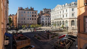 Une vue de rue avec des immeubles, une zone piétonne et une petite place avec des bancs.