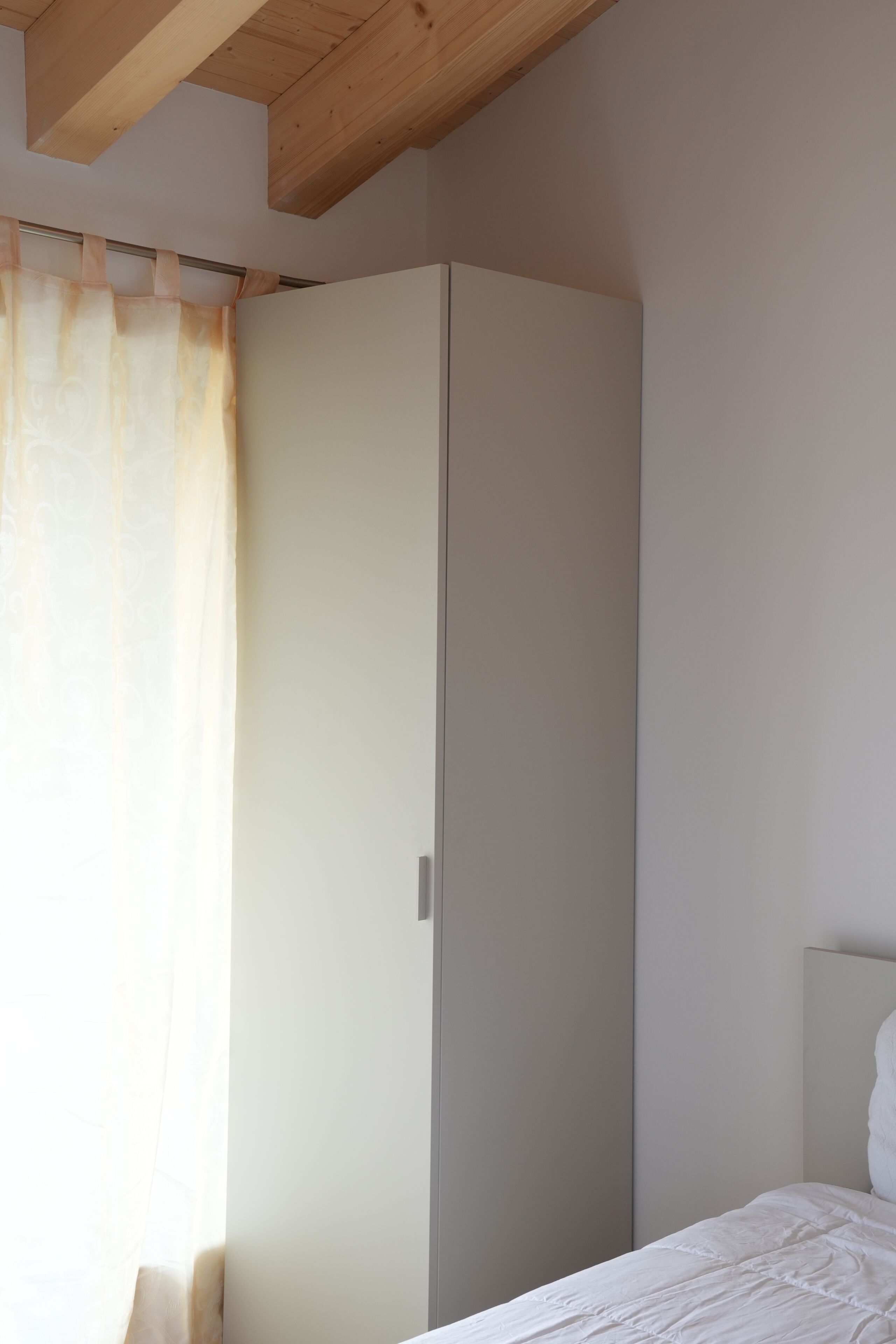 A bedroom with a bed, a wardrobe, and a window with curtains.