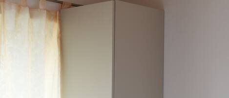 A bedroom with a bed, a wardrobe, and a window with curtains.