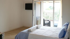 Ein Schlafzimmer mit Holzbalkendecke, einem Bett mit weißer Bettwäsche, einem an der Wand montierten Fernseher und einer Schiebeglastür, die zu einem Außenbereich führt.
