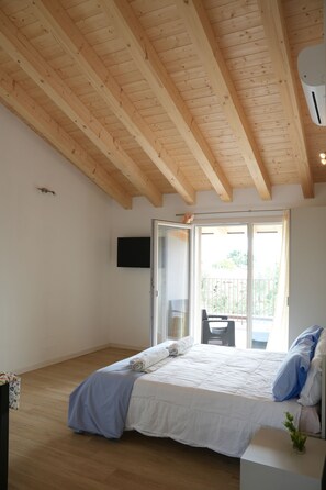 A bedroom with a wooden ceiling, a bed with white bedding, a TV on the wall, and a sliding glass door leading to an outdoor area. - Horizon View Apartment (Veneto)