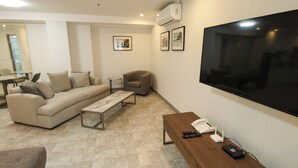A modern living room with a sofa, armchair, coffee table, and a TV mounted on the wall. - La Grande Residence - Deluxe Suite A (Angeles)