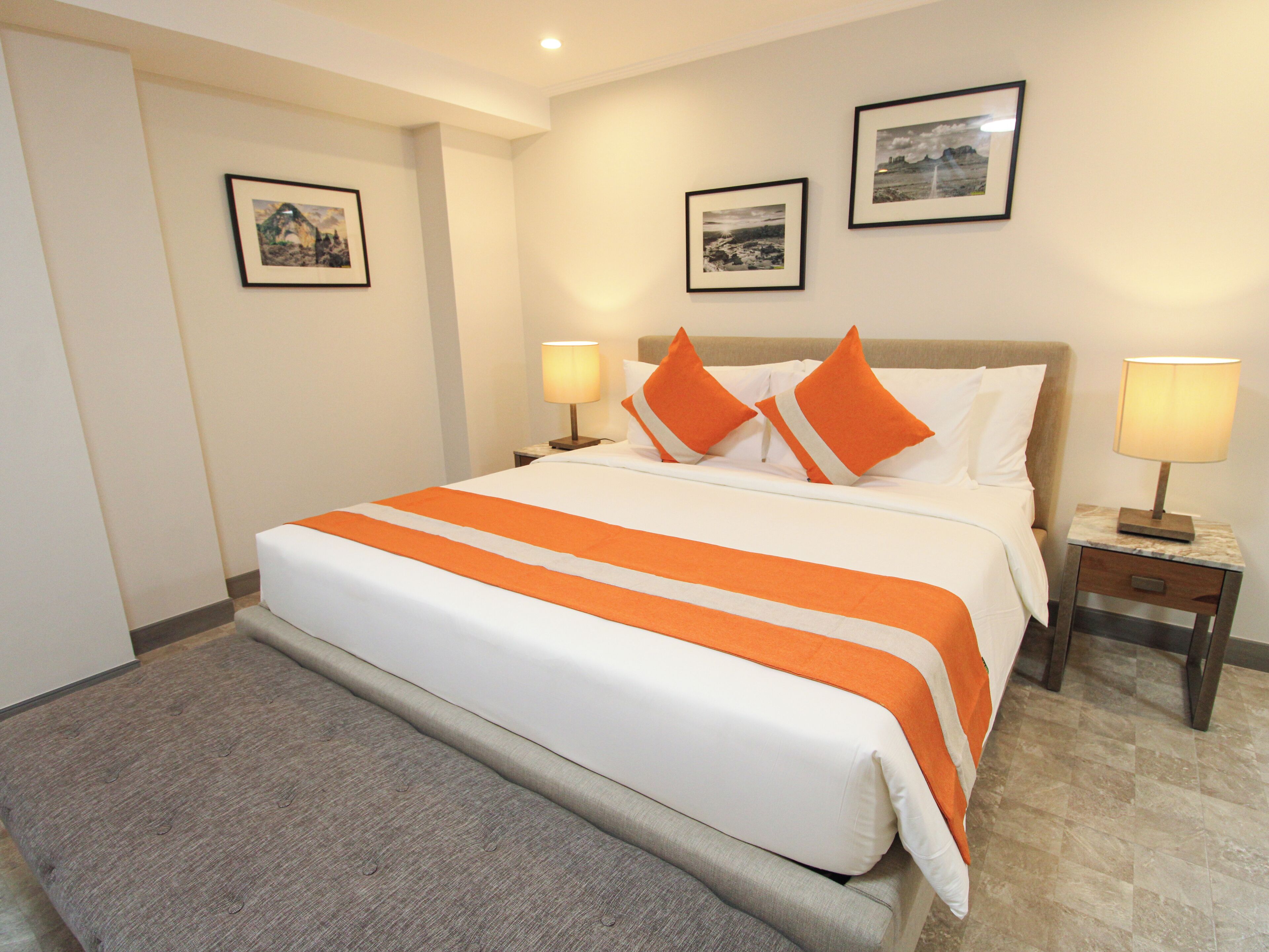 Habitación de hotel con una cama grande, dos mesitas de noche con lámparas y dos cuadros en la pared.