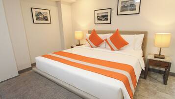 Habitación de hotel con una cama grande, dos mesitas de noche con lámparas y dos cuadros en la pared.