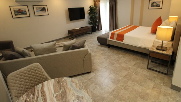 A hotel room with a bed, sofa, TV, and a marble table. - La Grande Residence - Deluxe Suite A (Angeles)