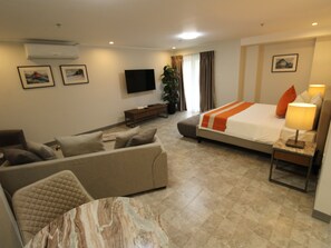 Una habitación de hotel con cama, sofá, televisión y una mesita de mármol.