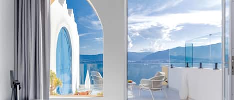 Un balcon avec vue sur un plan d’eau et des montagnes, une baignoire blanche et des fauteuils en osier.