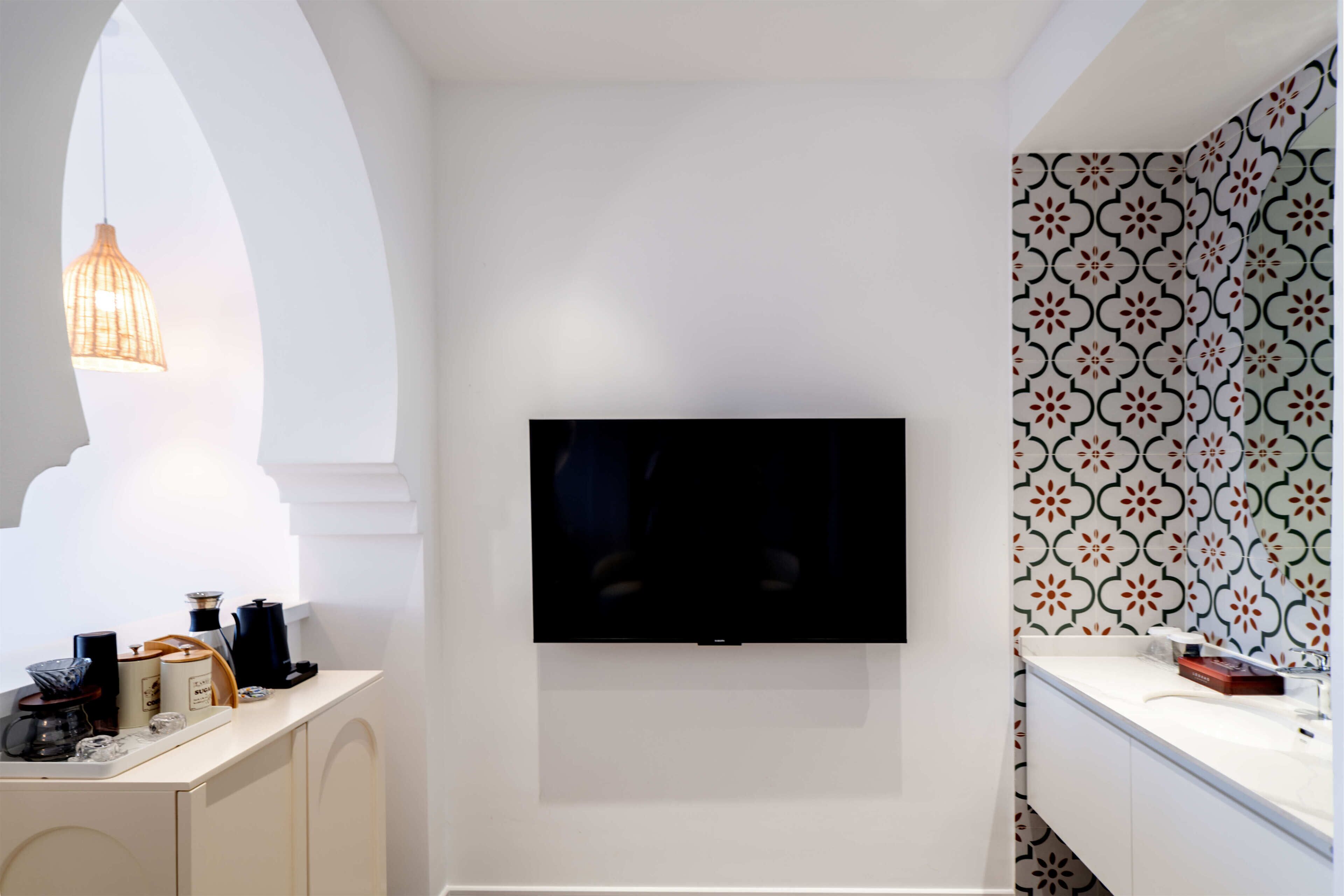 A modern bathroom with a flat-screen TV mounted on the wall, a white vanity, and patterned tiles.