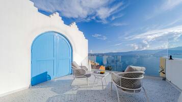 A balcony with a white wall, a blue door, and a view of the sea and cityscape.