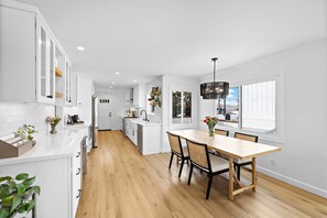 Eine moderne Küche mit weißen Schränken, einem Holztisch und einem großen Fenster.