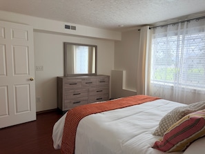 Un dormitorio con cama, cómoda, espejo y ventana con cortinas.