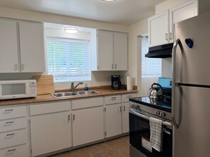 A modern kitchen with white cabinets, a stainless steel refrigerator, a microwave, a kettle, and a coffee maker.