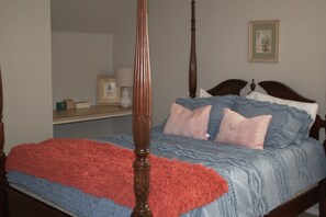 Ein Bett mit Baldachin, ausgestattet mit einer blauen und roten Bettdecke, einem hölzernen Kopfteil und einem Nachttisch mit Lampe.