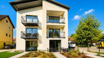 A modern multi-story building with balconies, a patio area with seating, and a well-maintained garden.