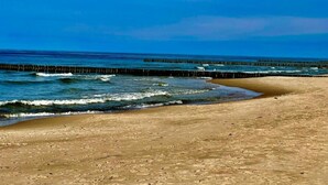 Een strand met een houten pier die zich uitstrekt over de oceaan, een zandstrand en een helderblauwe lucht.