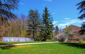 A garden with a clear path, a covered greenhouse, and a stone building with a red roof.