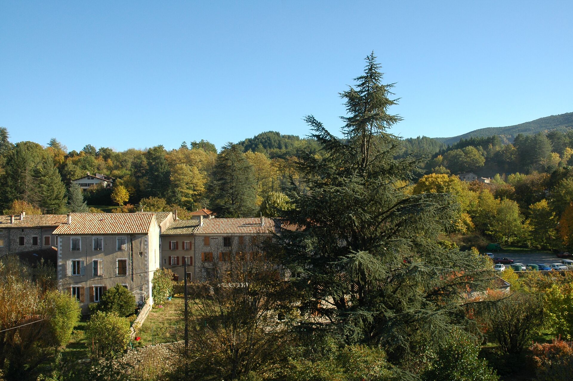 Un bâtiment à la façade en pierre et doté de nombreuses fenêtres, entouré d’arbres et situé dans un paysage vallonné.