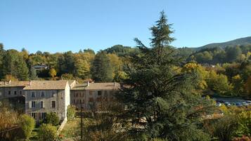Un bâtiment à la façade en pierre et doté de nombreuses fenêtres, entouré d’arbres et situé dans un paysage vallonné.