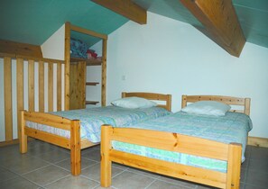 A bedroom with two wooden beds, a wooden wardrobe, and a slanted ceiling.