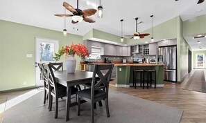 Uma cozinha moderna com uma ilha central, um espaço de refeições com mesa e cadeiras, e um ventilador de teto.