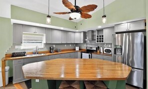 Uma cozinha moderna com ilha central, eletrodomésticos de aço inoxidável e ventilador de teto.