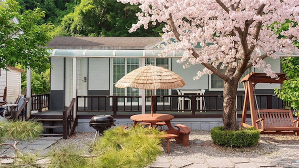 A patio with a grill, a table with an umbrella, and a cherry blossom tree.
