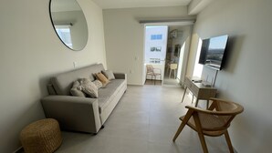Un salon avec un canapé, un fauteuil, un miroir rond et un téléviseur.