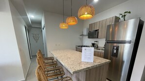 Une cuisine dotée d’un îlot central, d’appareils électroménagers en acier inoxydable, de tabourets de bar en osier et de luminaires suspendus.