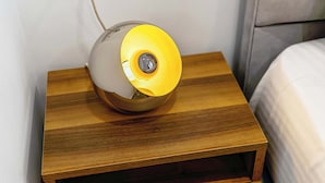 Een nachtkastje met een lamp, een bed en een muur.