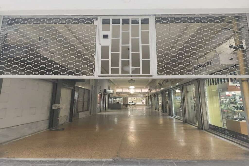 A corridor with a metal security gate, glass storefronts, and a tiled floor.