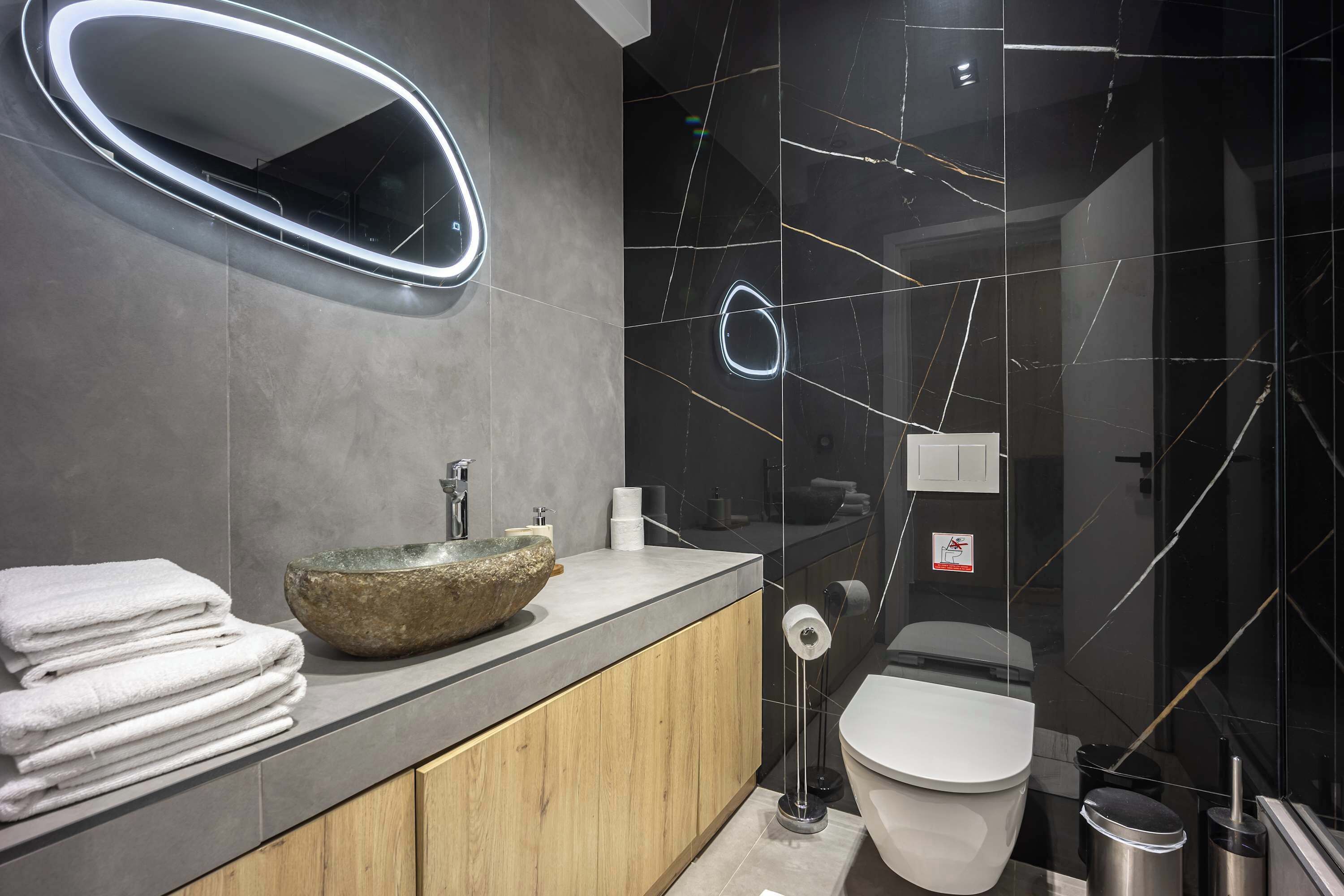 Une salle de bain moderne avec un lavabo en pierre, un miroir, des toilettes et une poubelle.